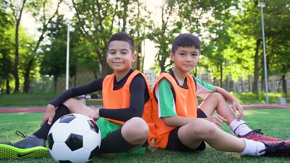 Football Players in Orange Vests Sitting on the Artificial Turf and Posing on Camera alt