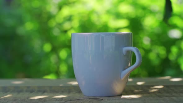 Hot Drink in a Cup Against the Background of a Summer Garden in the Morning alt