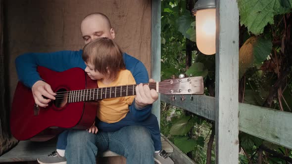 Dad Plays an Acoustic Guitar for His Small Child