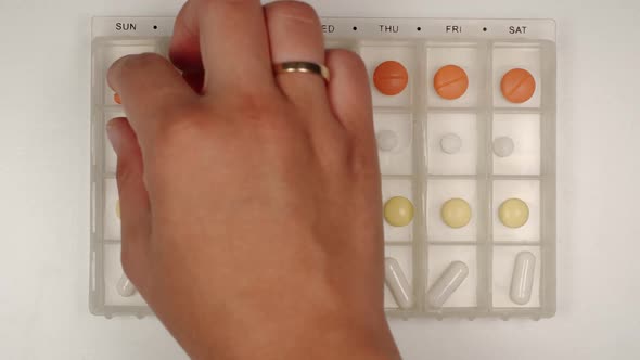 Female hand takes a pill from a pill organizer