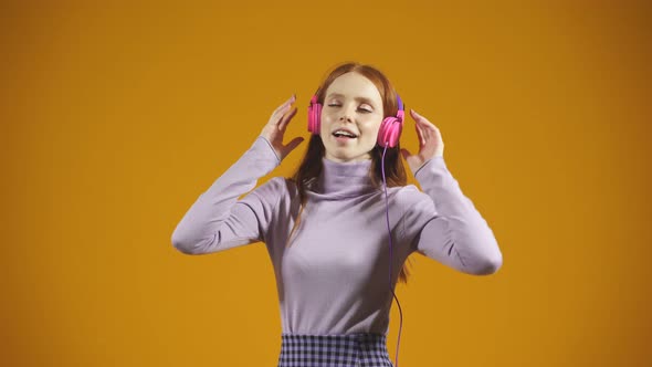 Portrait of a Young Woman Singing in a Studio on an Orange Background Listening to Music with