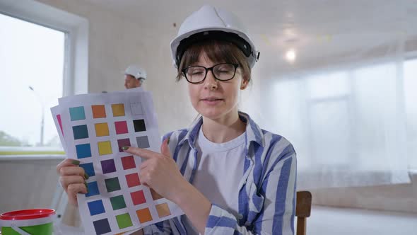 Woman in Hard Hat Discusses Wall Paint Using Color Palette with Customer Via Video Call on Laptop alt