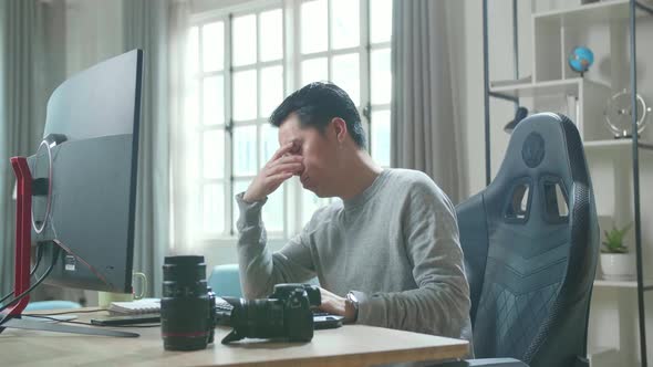 Asian Cameraman Tired While Using Desktop Computer For Working At Home alt
