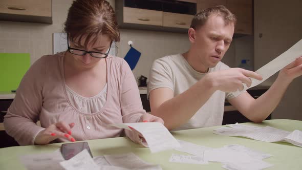 A married couple in the evening sitting at the table looks through the checks alt