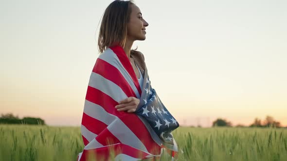 Portrait of Happy Mixed Race Young Woman Standing in Wheat Field Wrapped in USA National Flag alt