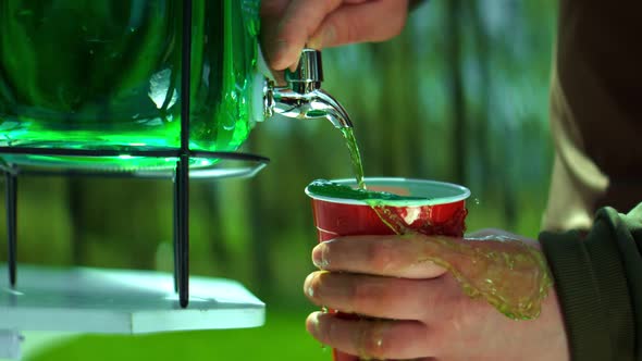 Pouring of Green Lemonade in a Cup in the Park