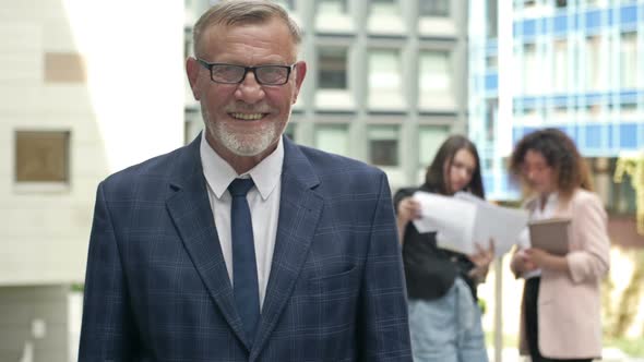 Portrait of a Smiling Senior Businessman in the Courtyard of a Large Business Center alt