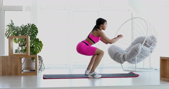 Black fit girl doing fitness aerobic exercises for booty in living room.