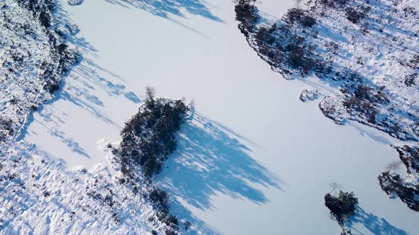 Aerial revealing birdseye view of snowy bog landscape with frozen lakes in sunny winter day, Dunika alt