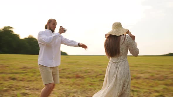 A Man Photographs a Woman in a Straw Hat on a Film Camera in a Field at Sunset