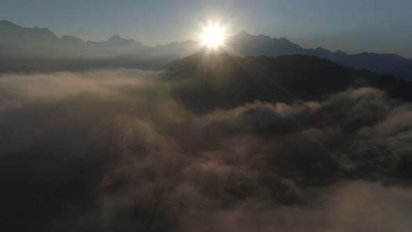 Flying Over the Clouds or Mist in Mountains in Backlight on Sunrise. Drone Shot