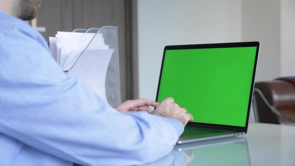 Man in the home office typing on laptop keyboard with green screen chroma mock-up alt