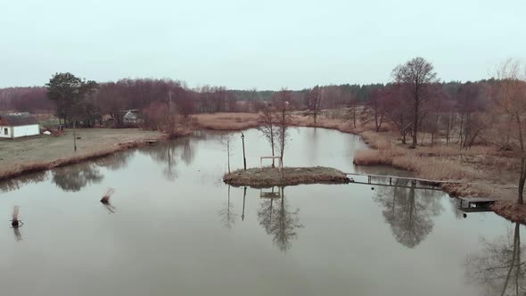 Small lake with village houses surrounded by tree forest, drone shot view alt