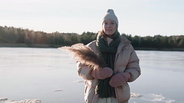 Stylish Woman Standing on a Frozen Lake on a Sunny Winter Day in Light Outfit