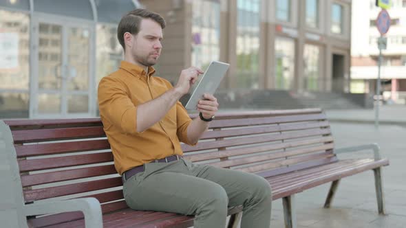 Young Man using Tablet while Sitting Outdoor on Bench alt
