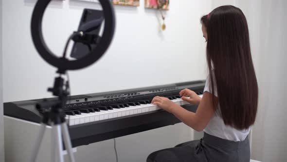 Child Girl Playing Music Keyboard Piano Instrument and Shoots a Video alt