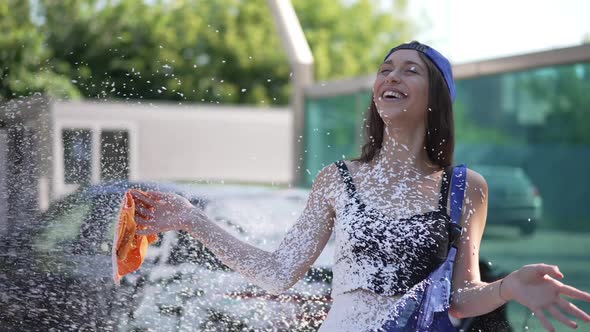 Young Joyful Woman Laughing As Car Wash Shampoo Spraying on Body in Slow Motion Outdoors alt