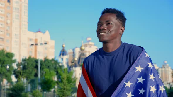 Smiling Afroamerican Man Walking Street with American Flag on Back in Summer alt