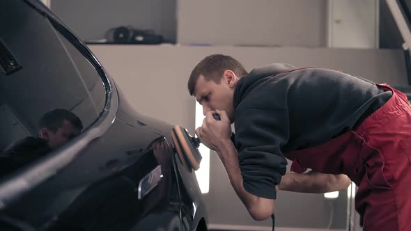 Young Male Worker Ofautocenter Takes Care of Black Expensive Car Polishing It with Rubbing Mashine alt