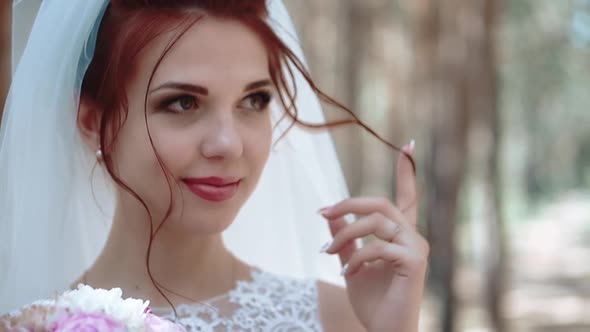 Portrait of a Bride in a Forest in a Wedding Dress That Touches a Curl of Her Hair Closeup Slow alt