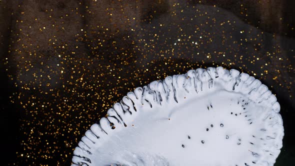 Drop of White Paint Spreads and Sprouts on a Golden Shimmering Background alt