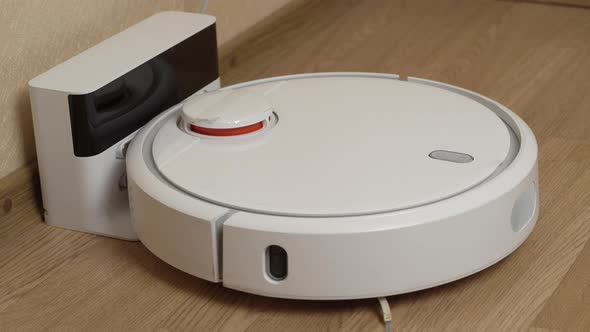 White Robotic Vacuum Cleaner Starts Cleaning From Its Charging Station alt