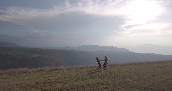 Aerial view of couple man and woman holding hands and whirling in field in mountains, Montenegro
