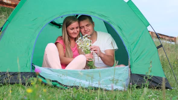 Loving man gave daisies while sitting in a tent while camping. alt
