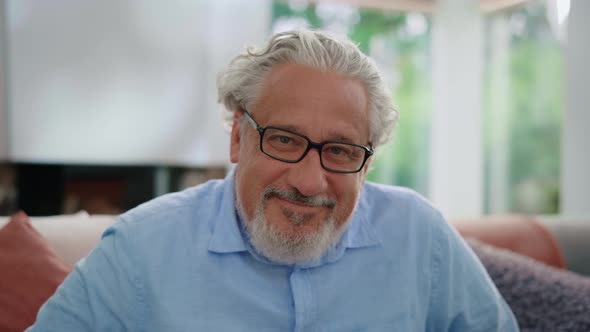 Senior Man Smiling at Camera. Portrait of Mature Man Sitting on Couch in Room alt