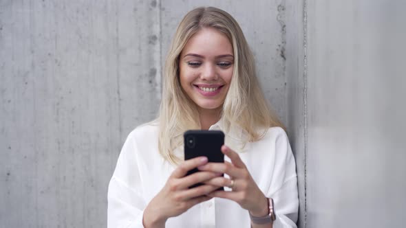Smiling Woman Using Smartphone Near Wall alt
