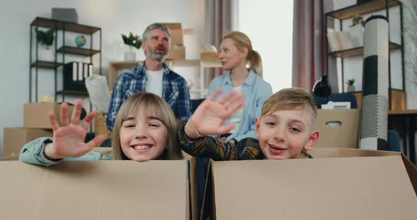 Boy and Girl Sitting in Carton Boxes and Waving Hands into camera alt