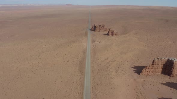 Aerial view going over a desert road toward a small rock group formation off the side of a Utah high alt