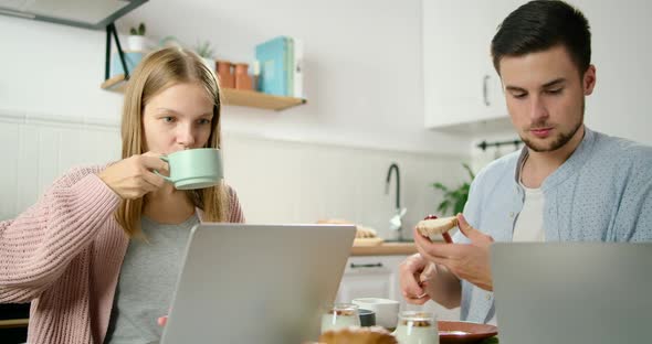 Young Couple Eat Breakfast and Work on Laptops in Kitchen in Home Office