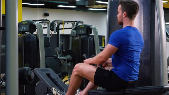 A Young Fit Man Trains on a Rowing Machine in a Gym alt