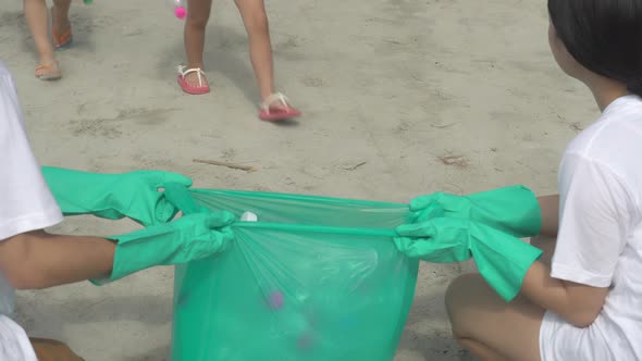Happy asian family team volunteer keeping garbage and plastic bottle while cleaning on beach. alt