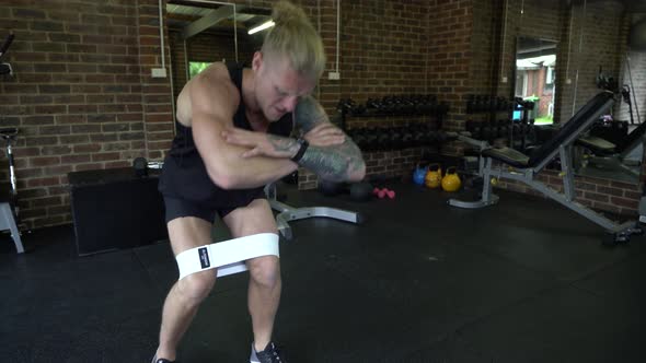 Tattooed man in home gym squat walk with resistance bands and finish alt