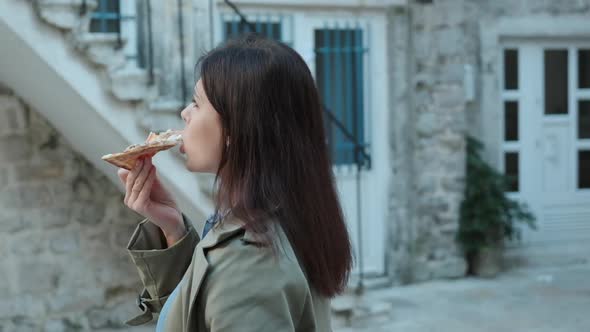 Slow motion Pretty young women in green coat walking and eating pizza in old town in spring time alt