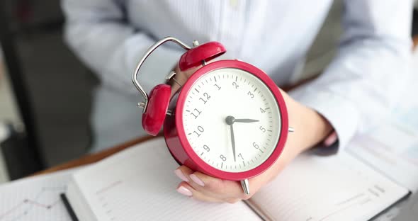 Businesswoman Translates Red Alarm Clock Back at Workplace alt