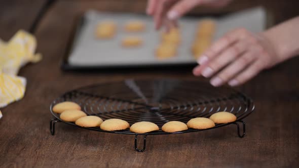 Pastry chef woman putting small vanilla cookies on a cooling rack.