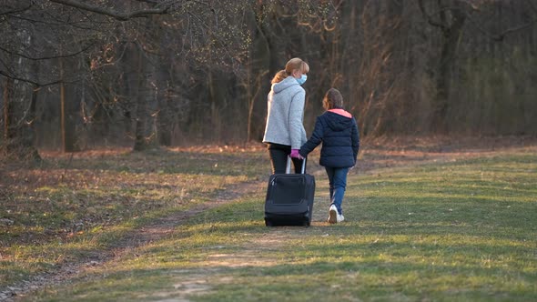 Mother and daughter walk through the spring Park in medical masks with a suitcase.