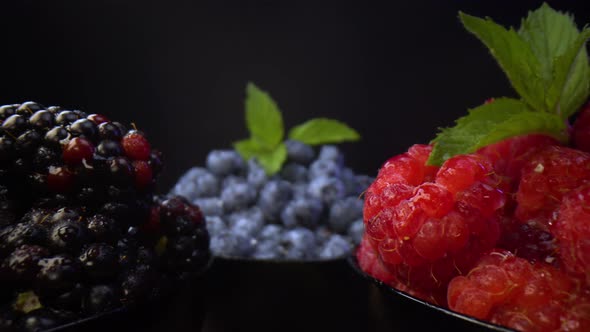 Fresh forest fruits. Blackberries, blueberries, raspberries in black bowls on a black background