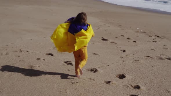 Little Girl with Flag of Ukraine Running on the Sandy Beach