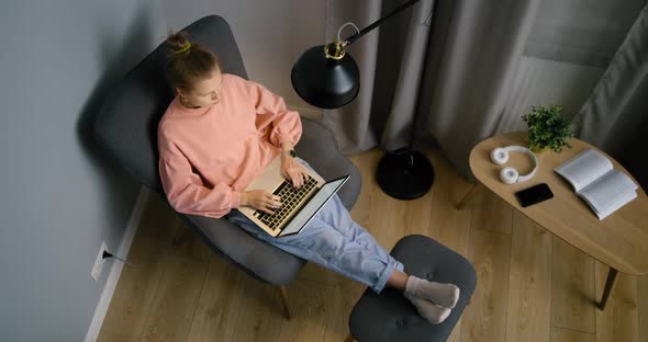Top View of Young Woman Working on Laptop at Home at Night in Armchair in Room