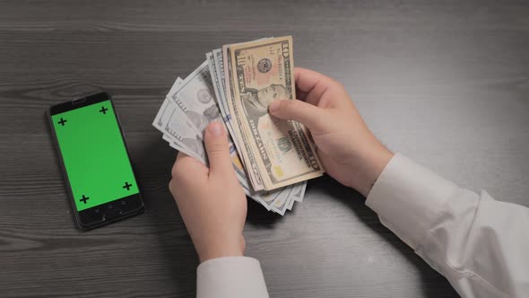 Businessman Counting Money and Green Screen Phone Laying Nearby on the Table alt