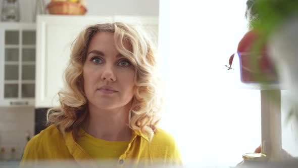 curly young woman opens refrigerator with healthy food and takes an apple Video 4k alt