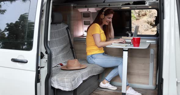 Senior caucasian woman using laptop and wireless headphone inside mini van camper alt
