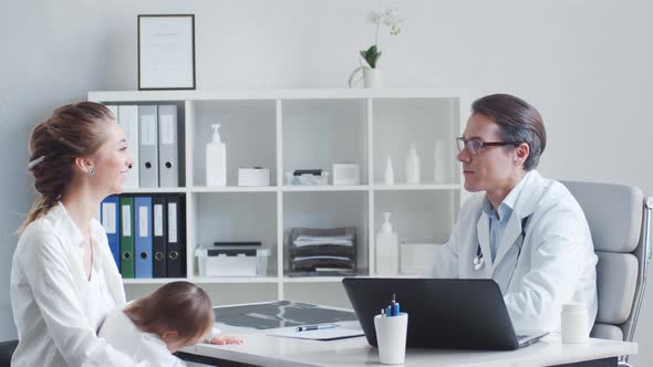 Male pediatrician is examining little baby. Doctor, mother and daughter in medical office. alt