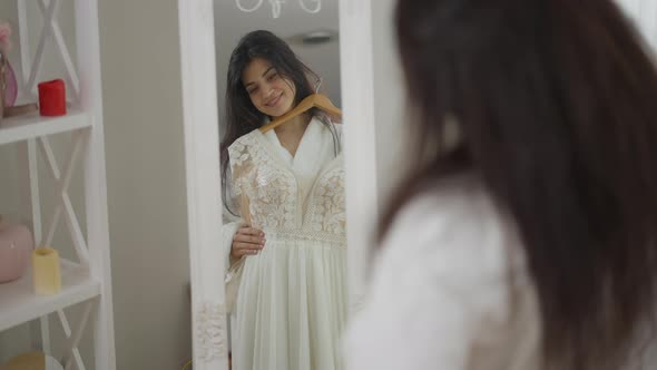 Reflection in Mirror of Smiling Happy Middle Eastern Bride Trying on Wedding Dress in the Morning alt