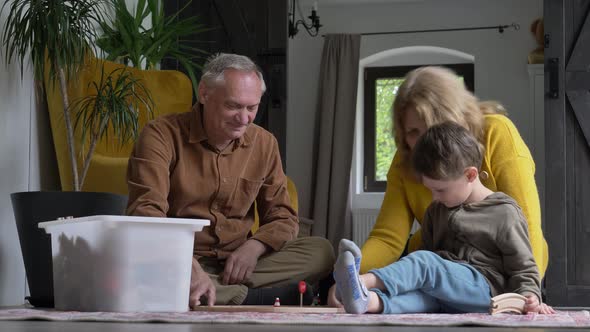 grandparents play the railway with their grandson at home.