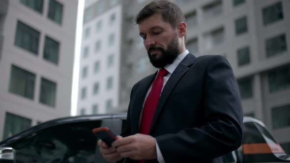 Serious Middleaged Businessman in Luxurious Clothes in the Financial District of a Metropolis Uses a alt